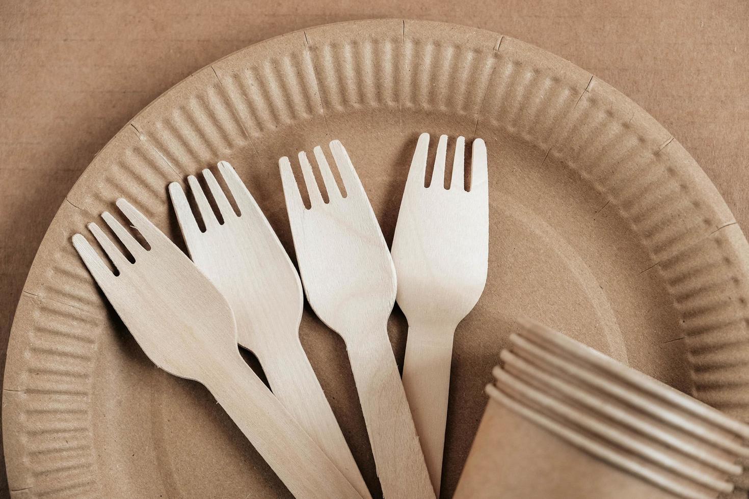 Wooden forks and paper cups with plates on kraft paper background. Eco friendly disposable tableware. Also used in fast food, restaurants, takeaways, picnics. Top view. Copy, empty space for text photo