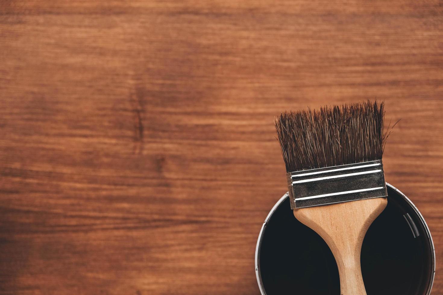 Open can of paint with brown brush on it on wooden background photo