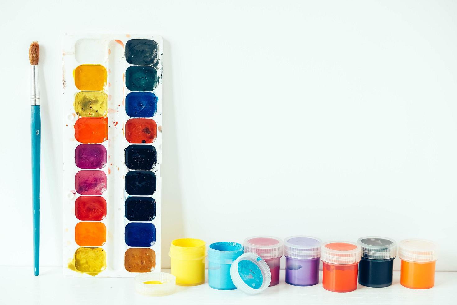 Colorful gouache paints and brush for painting on white wooden table. Copy, empty space for text photo