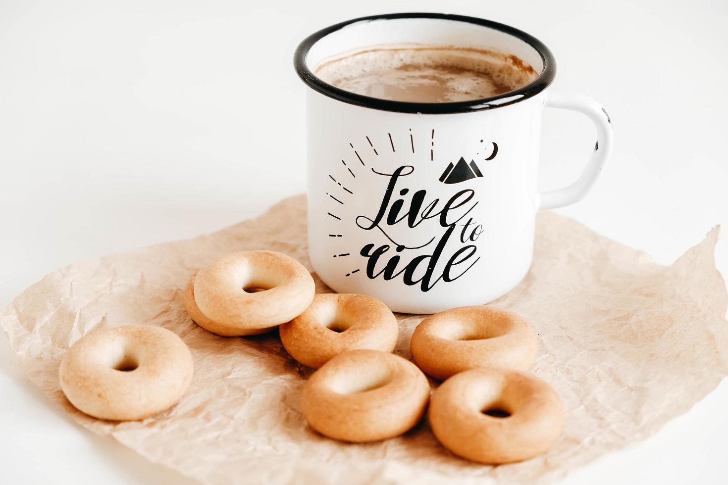 Metal mug with hot drink and mini round bagels on a white wooden background. Copy, empty space for text photo