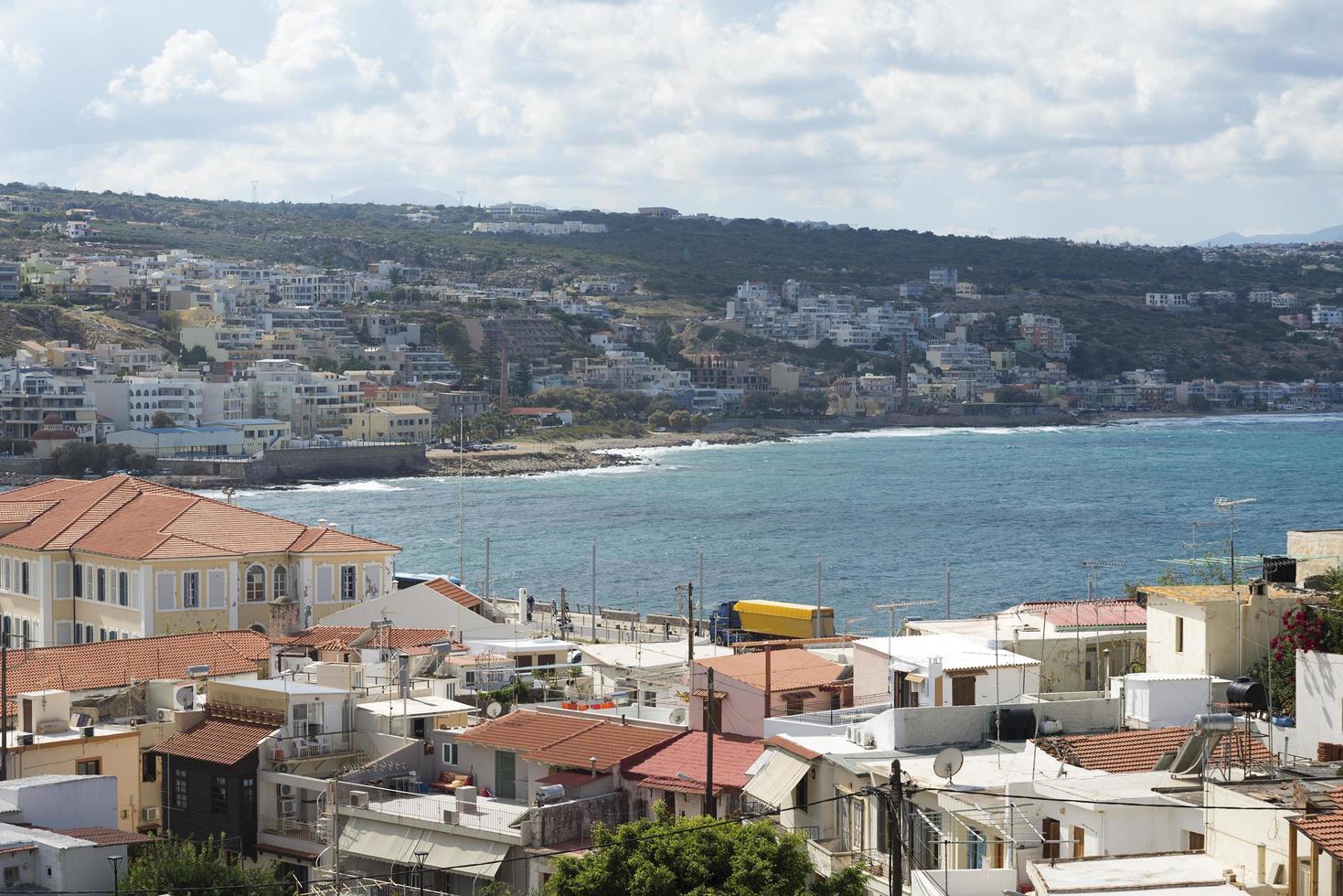 vista del complejo arquitectura griega ciudad-puerto de rethymno, construida por venecianos, desde la altura del castillo de fortezza - fortaleza en la colina paleokastro. techos de tejas rojas y montañas en el fondo. Creta. foto