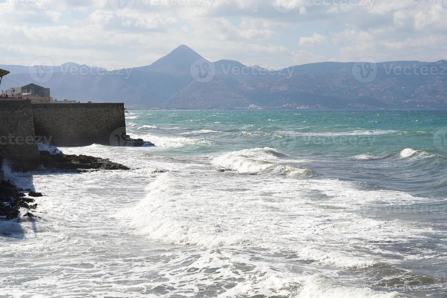 The waves breaking on a stony beach, forming a spray. Wave and splashes on beach. Waves crashing onto rocks. photo