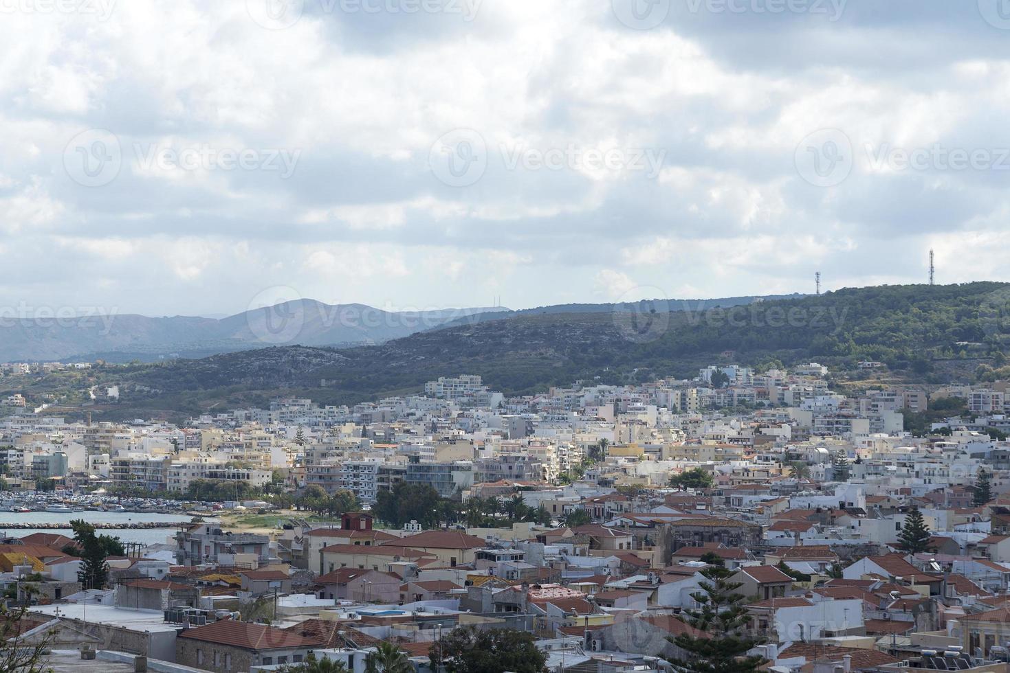 vista del complejo arquitectura griega ciudad-puerto de rethymno, construida por venecianos, desde la altura del castillo de fortezza - fortaleza en la colina paleokastro. techos de tejas rojas y montañas en el fondo. Creta. foto