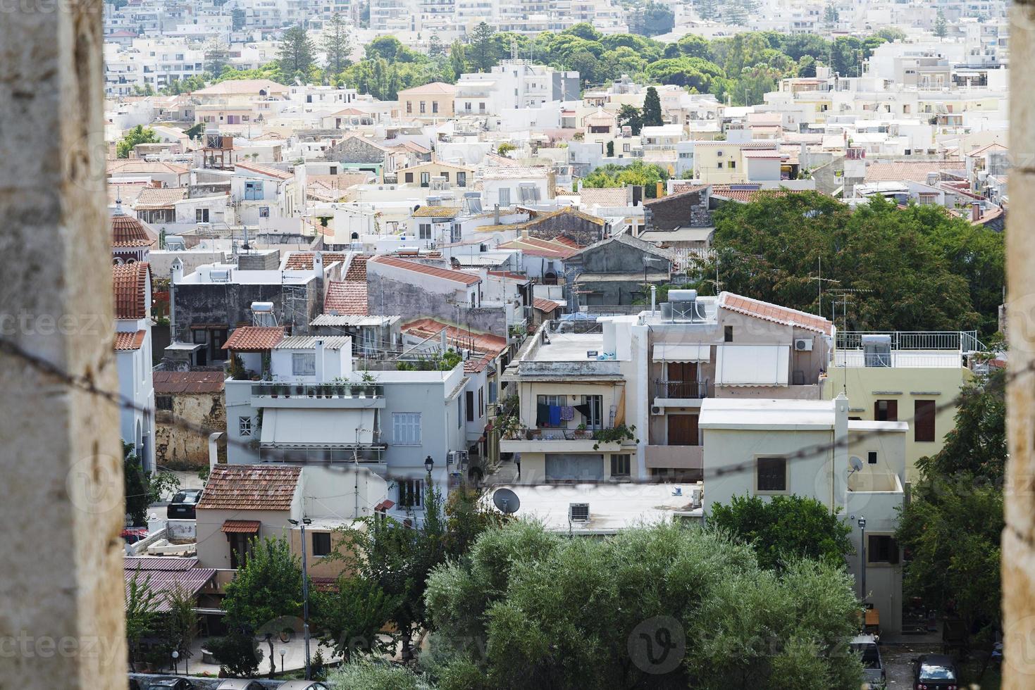 vista del complejo arquitectura griega ciudad-puerto de rethymno, construida por venecianos, desde la altura del castillo de fortezza - fortaleza en la colina paleokastro. techos de tejas rojas y montañas en el fondo. Creta. foto