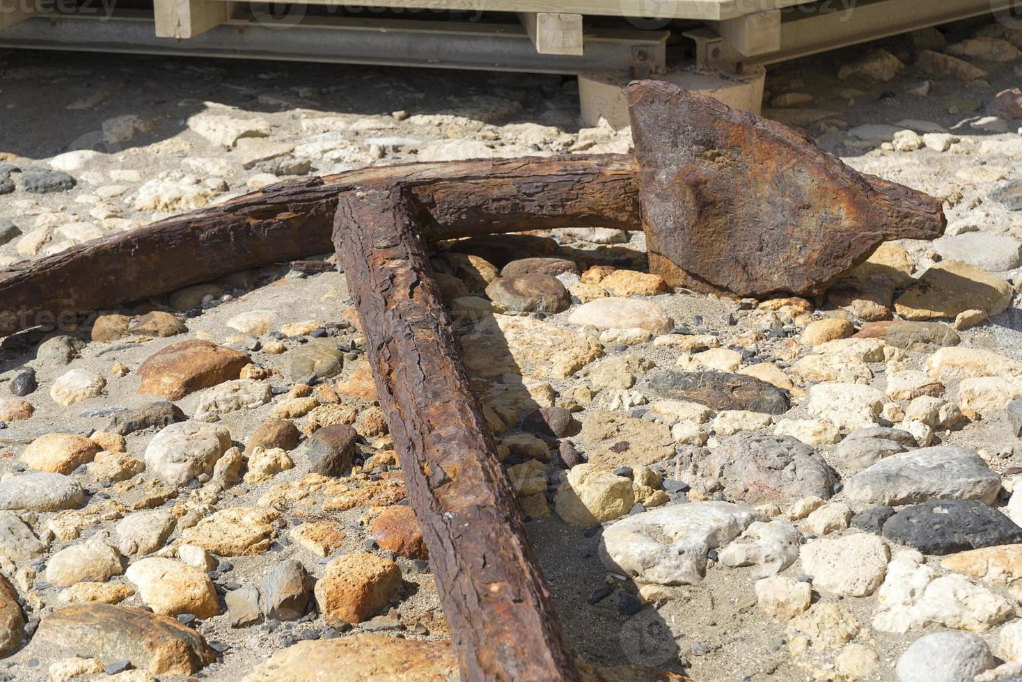 Old anchor lies on stones. Sunny day photo