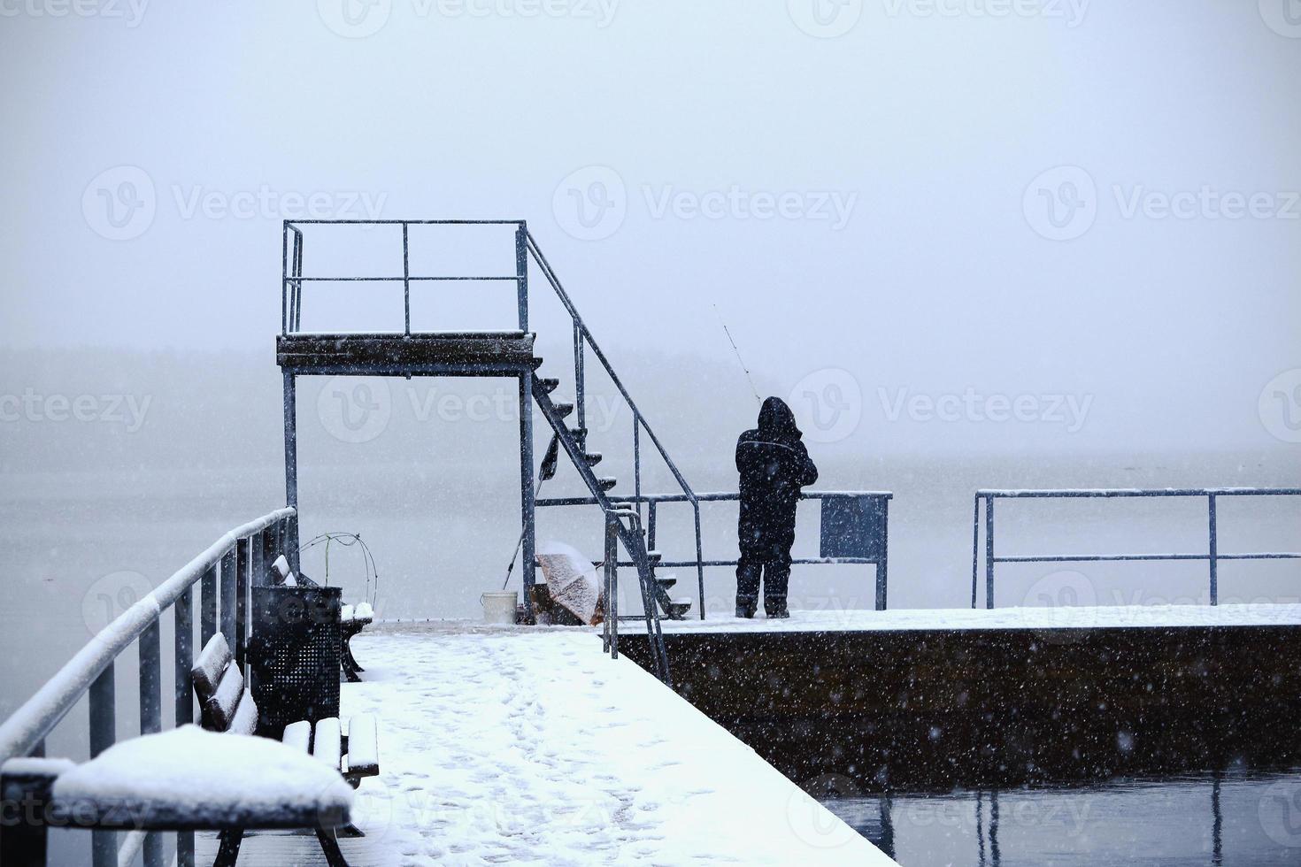 Old fisherman with a pole fishing in winter lake photo