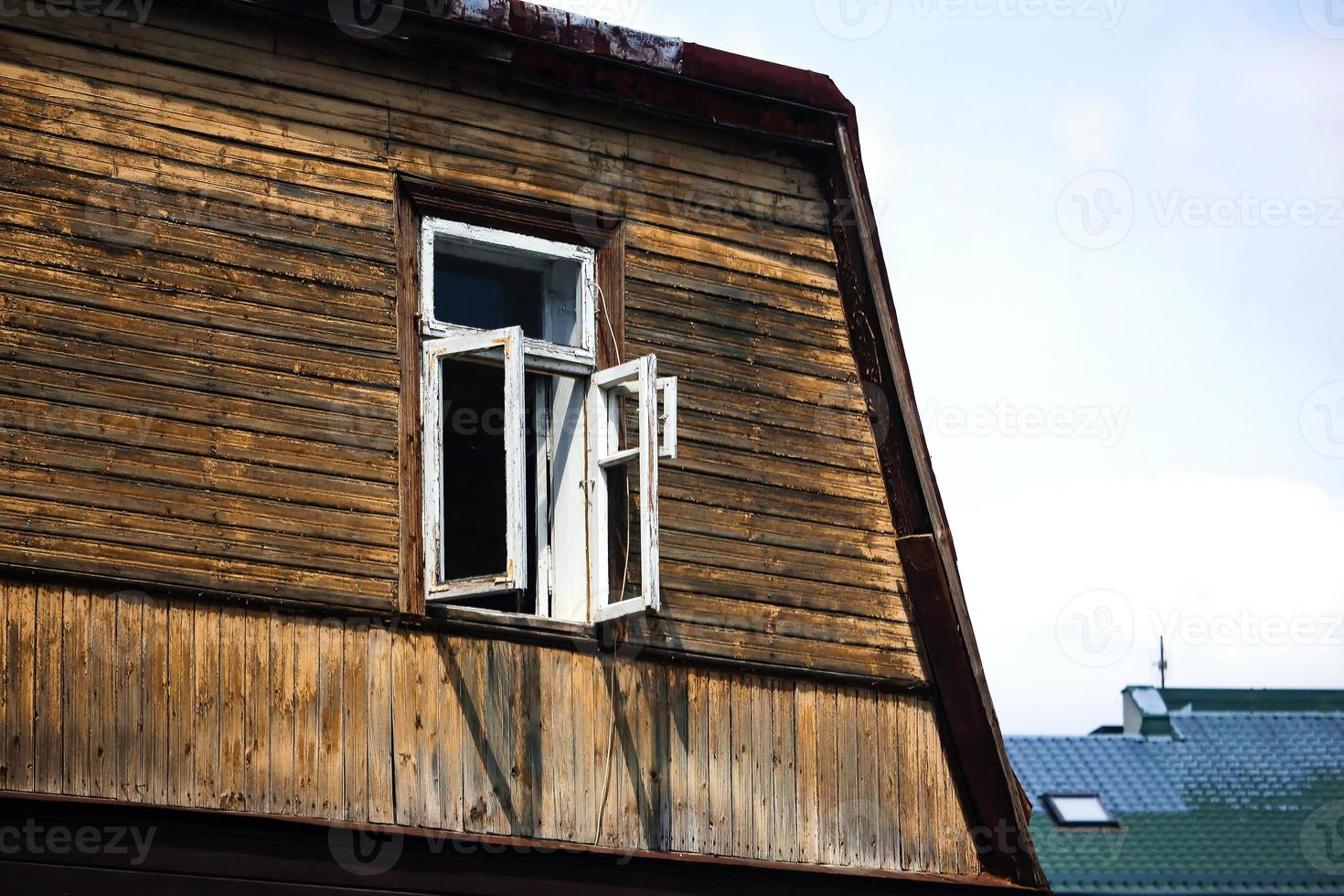 Dark wood building wall with open white window on blue sky background photo