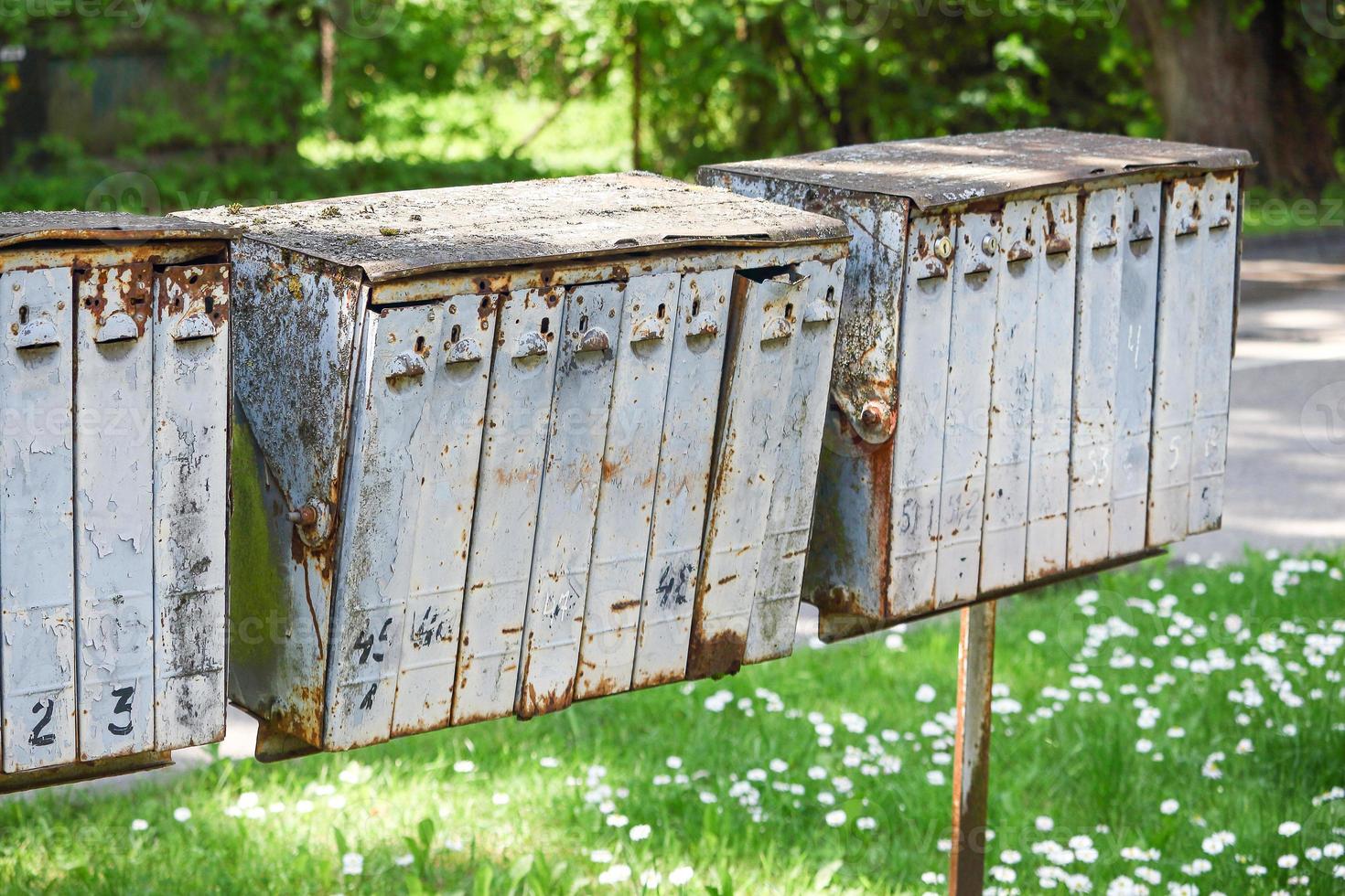 Old gray rusty mail boxes in empty garden yard with green grass photo