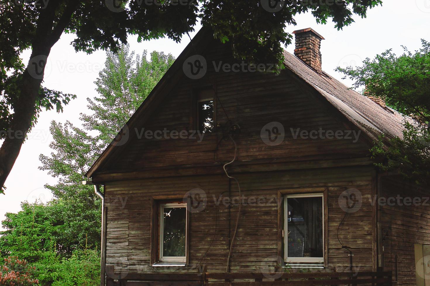 Old wooden house standing under a tree surrounded by greenery photo