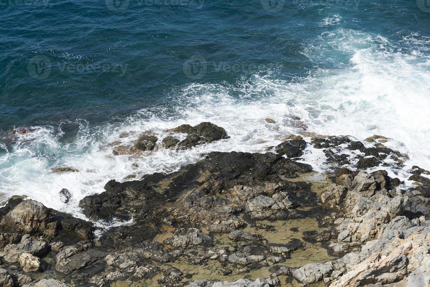 The waves breaking on a stony beach, forming a spray. Wave and splashes on beach. Waves crashing onto rocks. photo