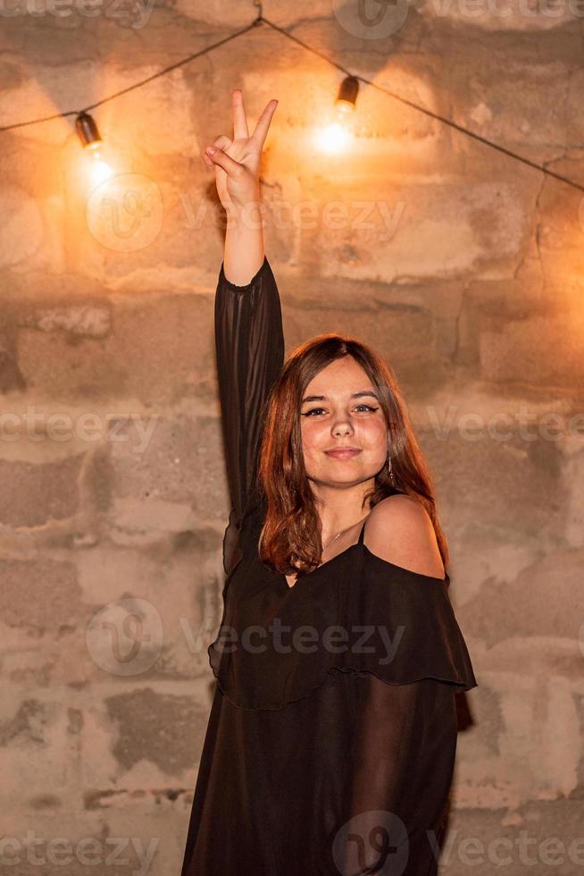 A teenage girl near the wall with flashlights in black dress. The girl has a positive cheerful mood. photo