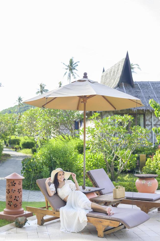 A young woman relaxing and sitting on the lounge chair looking at beautiful beach on holidays photo