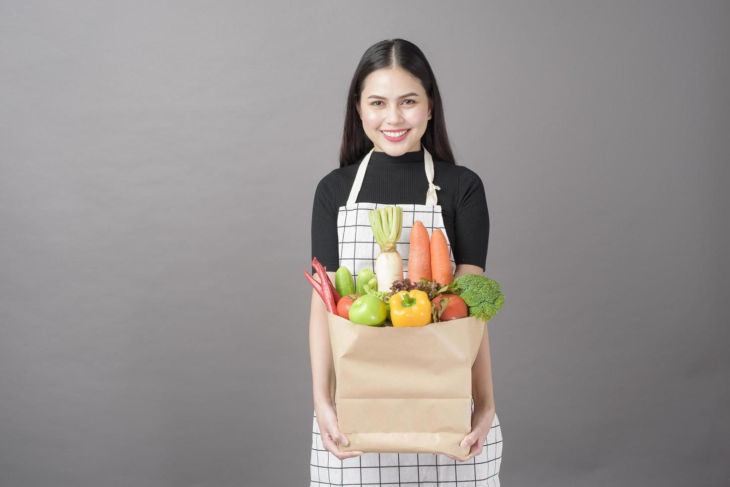 Portrait of beautiful young woman with vegetables in grocery bag in studio grey background photo