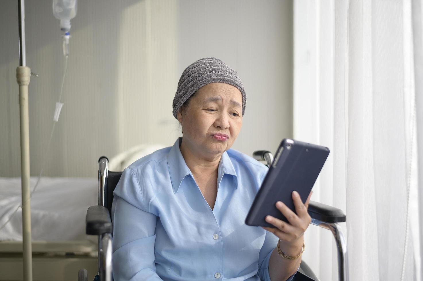 Cancer patient woman wearing head scarf making video call on social network with family and friends in hospital. photo