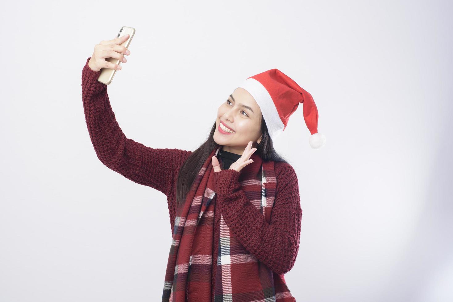 Young smiling woman wearing red Santa Claus hat taking a selfie on white background studio. photo