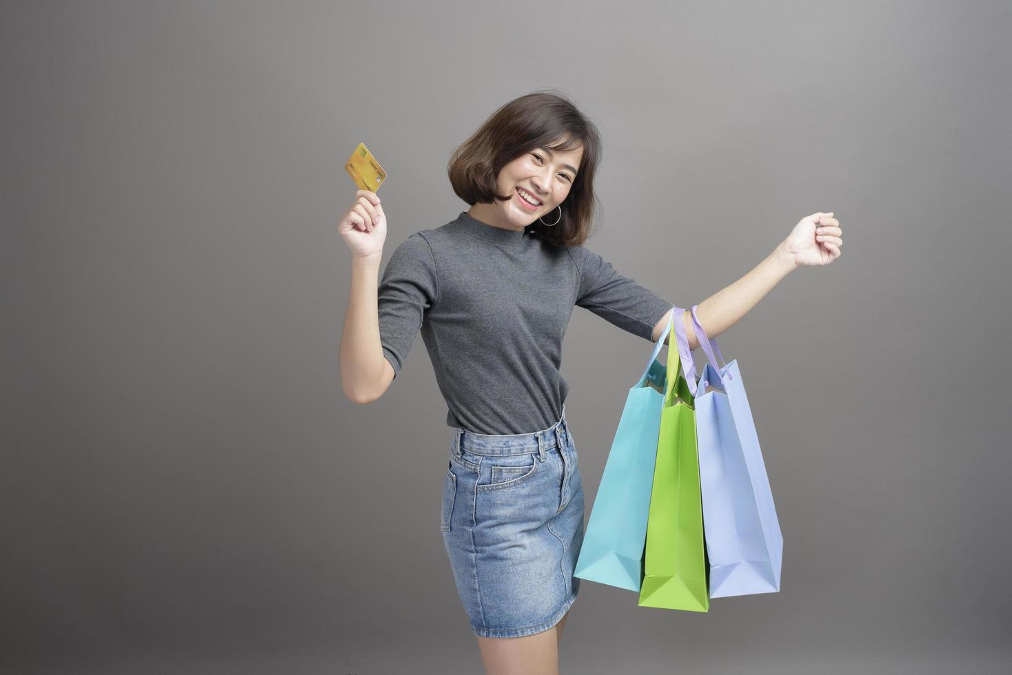 Portrait of young beautiful asian woman holding credit card and colorful shopping bag isolated over gray background studio photo