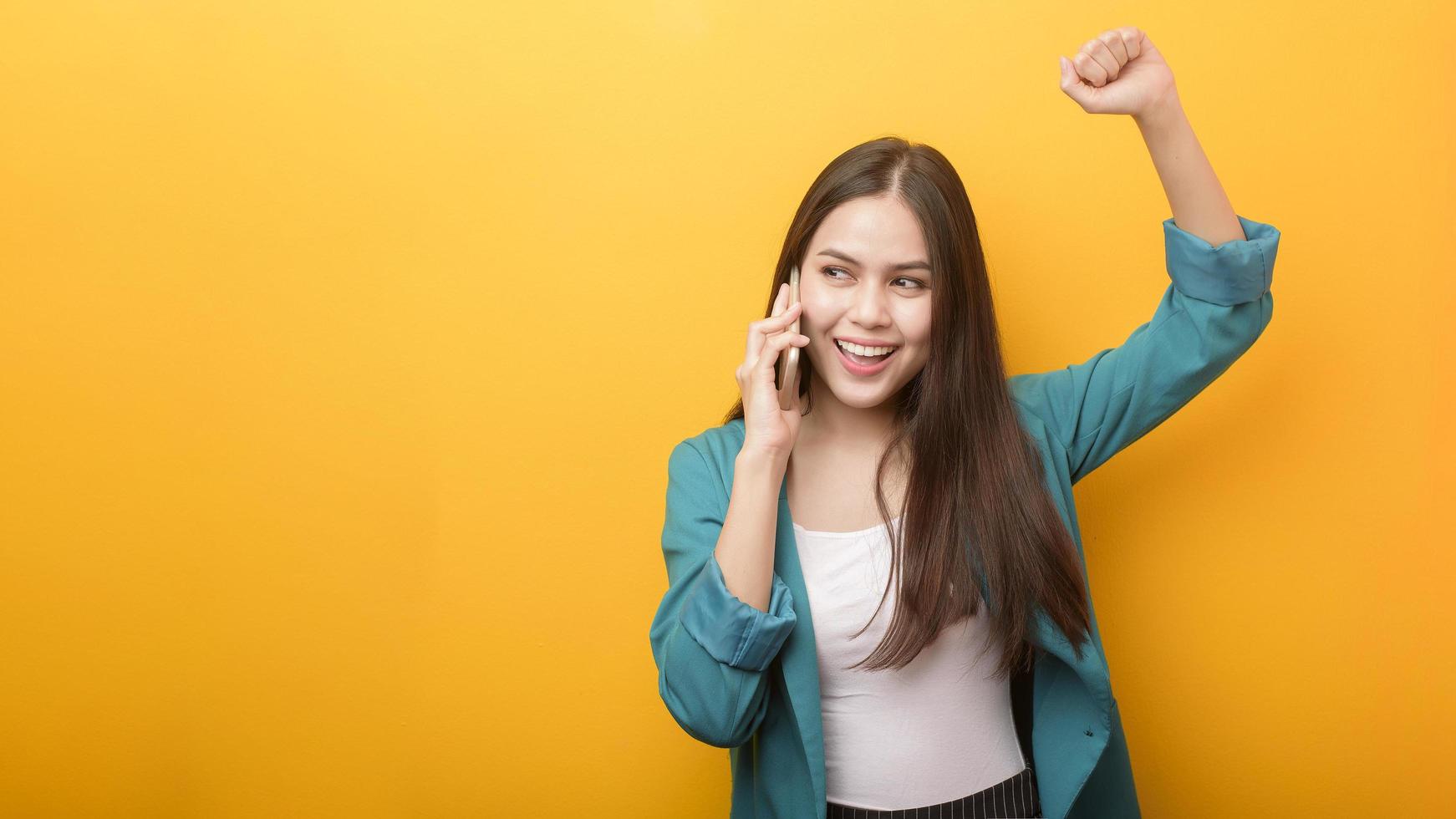 Fashion portrait of beautiful woman in green suit  using cellphone on yellow background photo