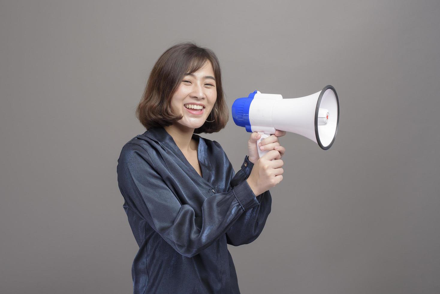 Portrait of young beautiful asian woman holding megaphone over studio background. photo