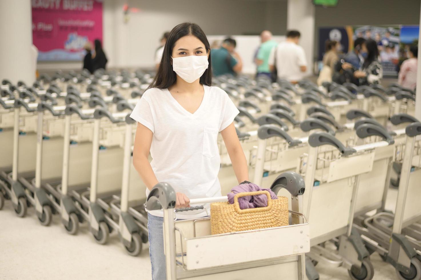 una mujer viajera con máscara protectora en el aeropuerto con equipaje en carro, viaje bajo la pandemia de covid-19, viajes de seguridad, protocolo de distanciamiento social, nuevo concepto de viaje normal foto