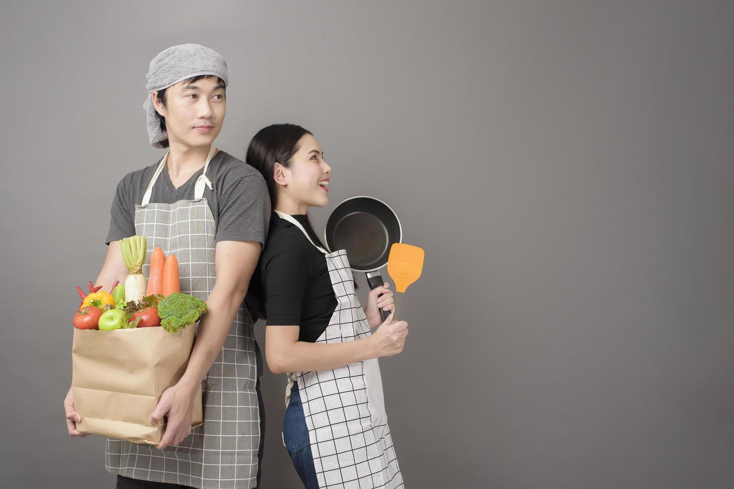 Happy couple is holding vegetables in grocery bag in studio grey  background photo
