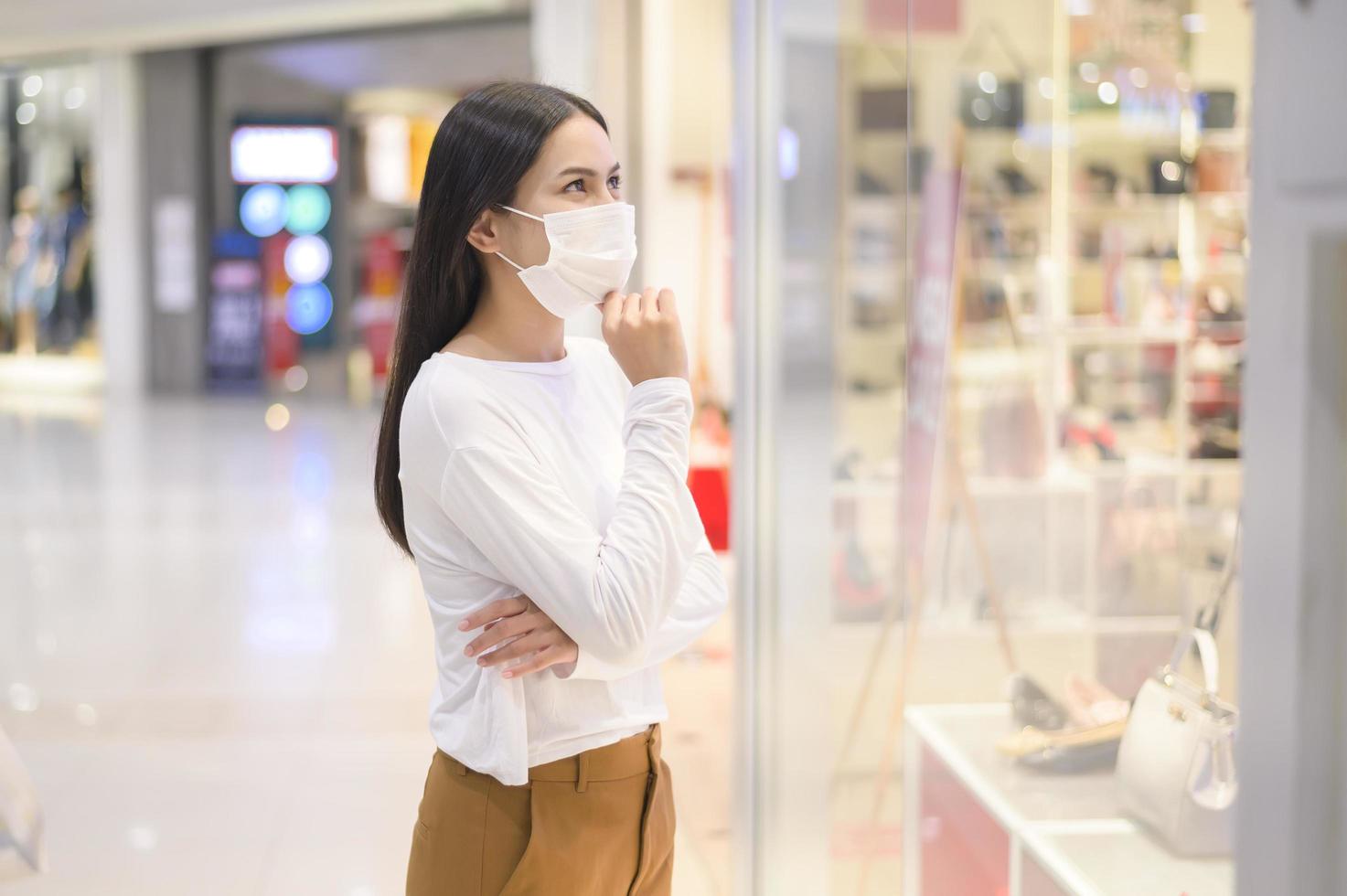 Woman wearing protective mask shopping under Covid-19 pandemic in shopping mall, social distancing protocol, New normal concept. photo