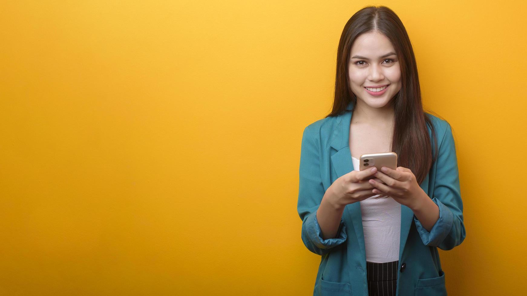 retrato de moda de una mujer hermosa con traje verde usando un celular con fondo amarillo foto