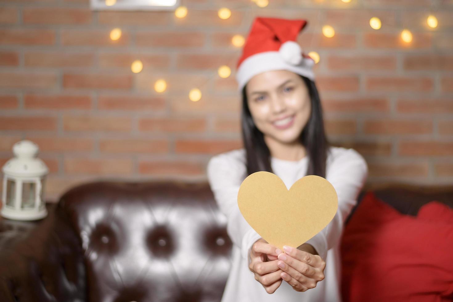 Young smiling woman wearing red Santa Claus hat showing a heart shaped model on Christmas day, holiday concept. photo