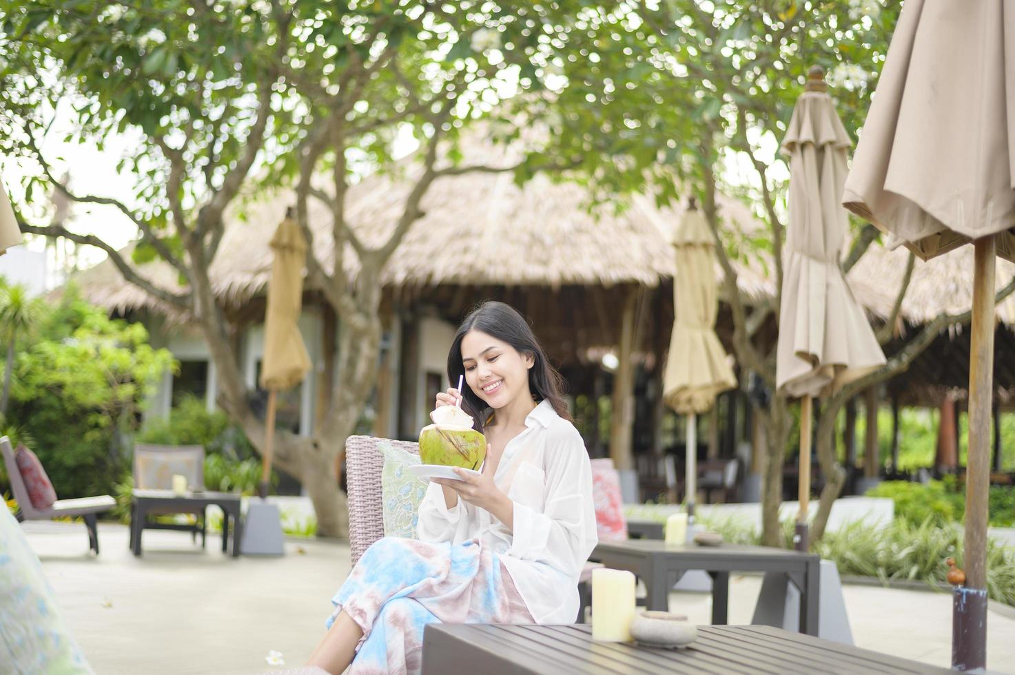 Beautiful woman tourist with white flower on her hair drinking coconut sitting on lounge chair during summer holidays photo