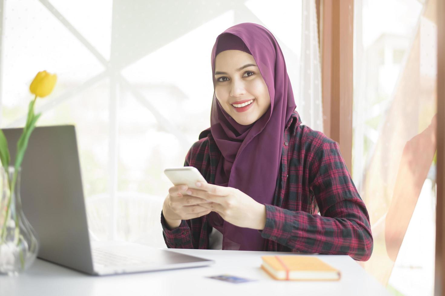 mujer musulmana con hiyab está trabajando con una computadora portátil en una cafetería foto