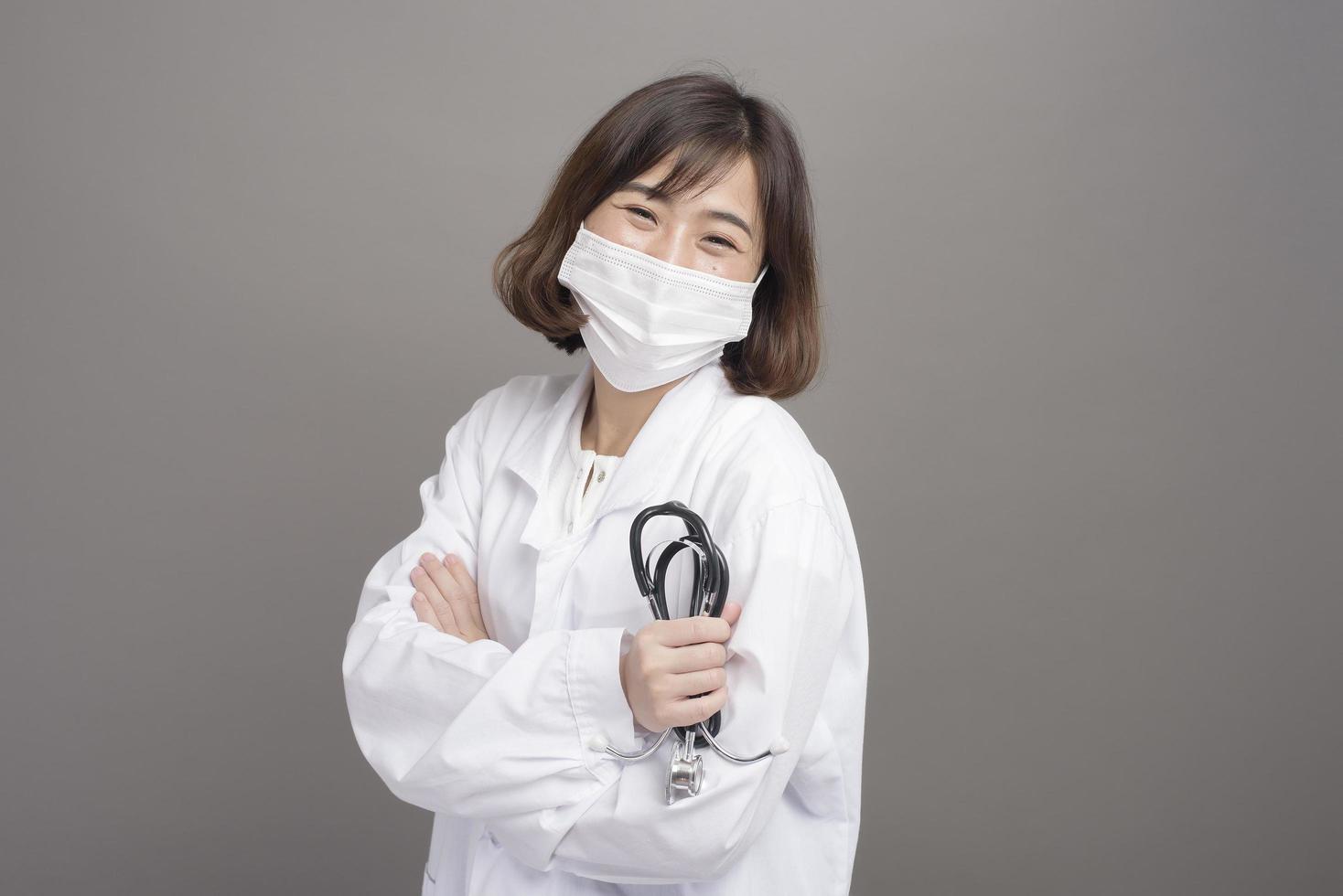 Young confident woman doctor is wearing surgical mask over grey background studio photo