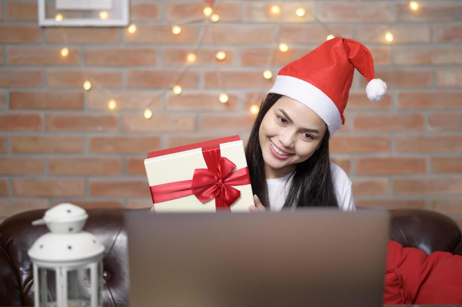 Young smiling woman wearing red Santa Claus hat making video call on social network with family and friends on Christmas day. photo