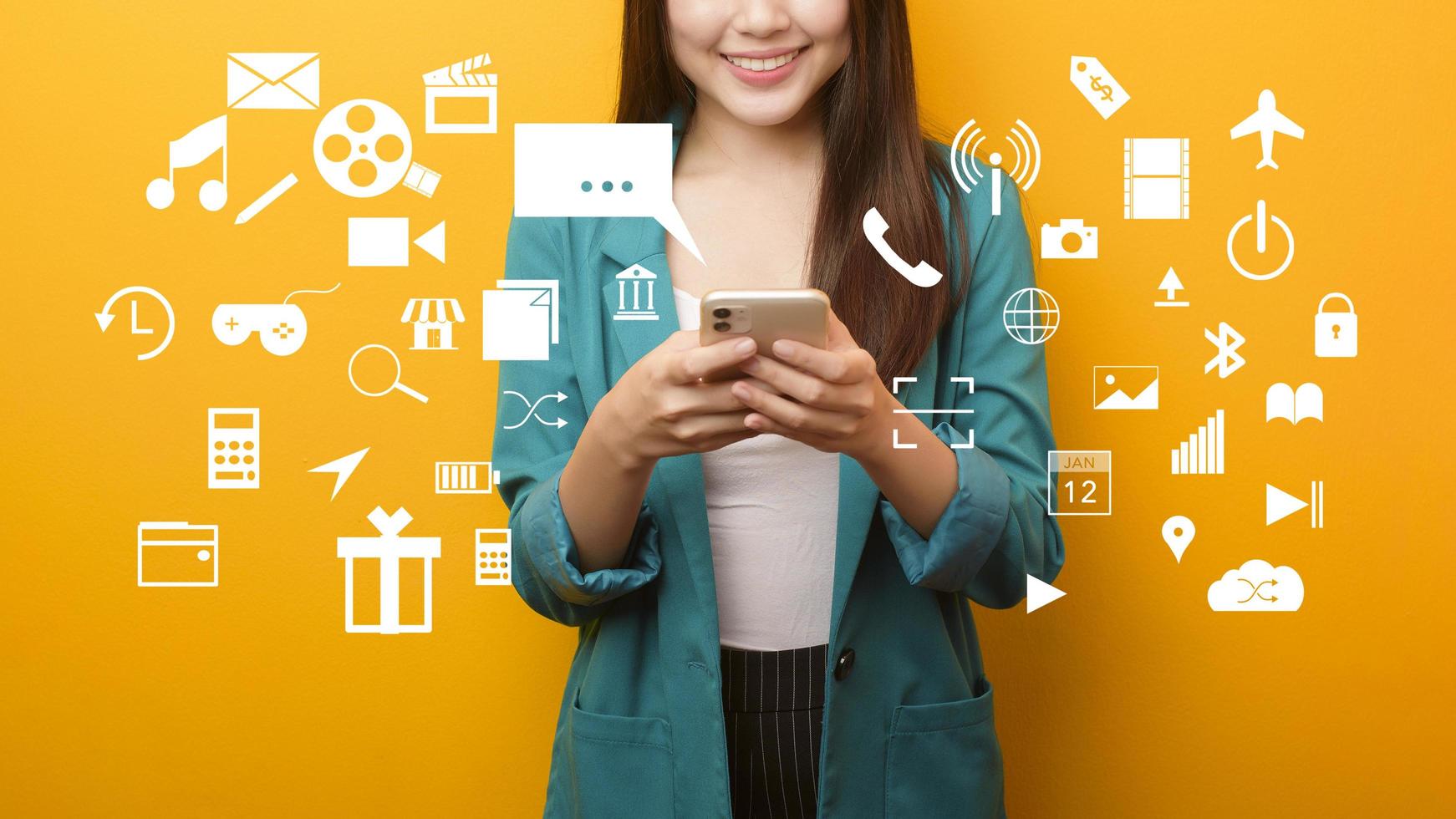 mujer con traje verde usando un celular con fondo amarillo con íconos multimedia foto