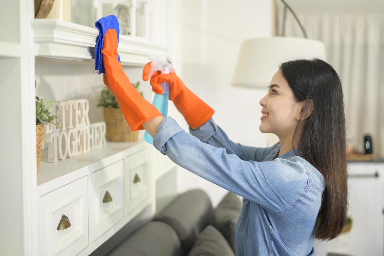 una mujer con guantes de limpieza que usa desinfectante en aerosol de alcohol para limpiar la casa, saludable y médica, concepto de protección covid-19 en el hogar foto