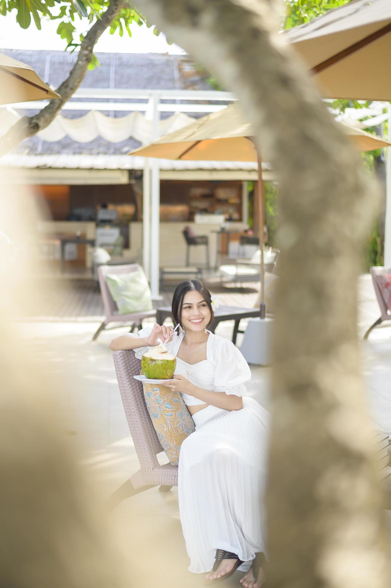 bella mujer turista con flor blanca en el pelo bebiendo coco sentada en un sillón durante las vacaciones de verano foto