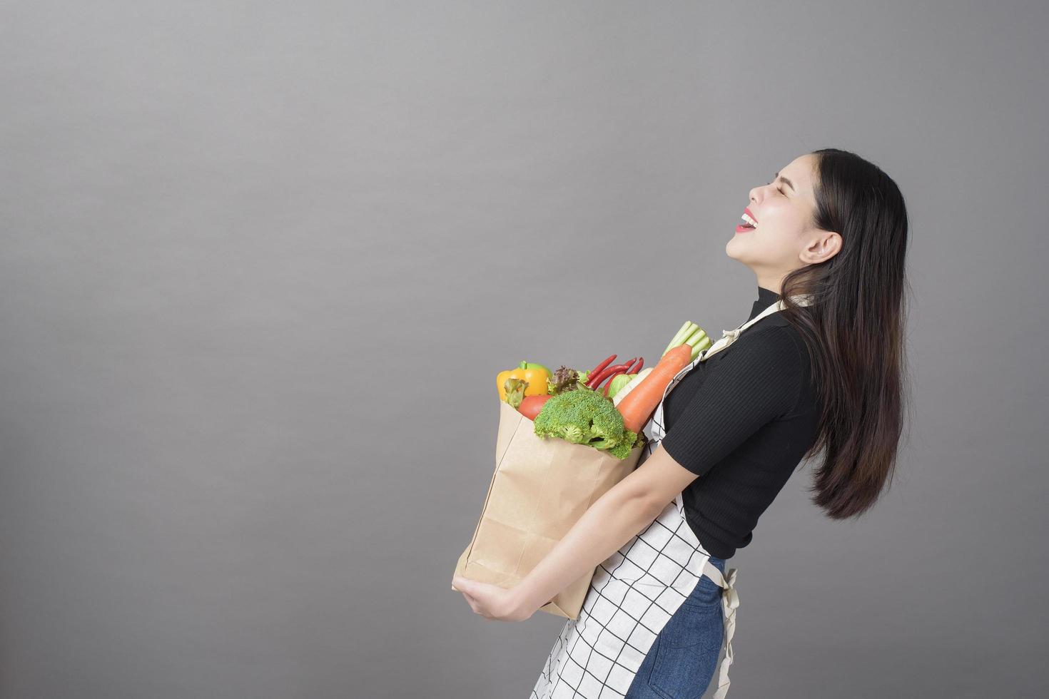 retrato de una hermosa joven con verduras en una bolsa de supermercado en un estudio de fondo gris foto