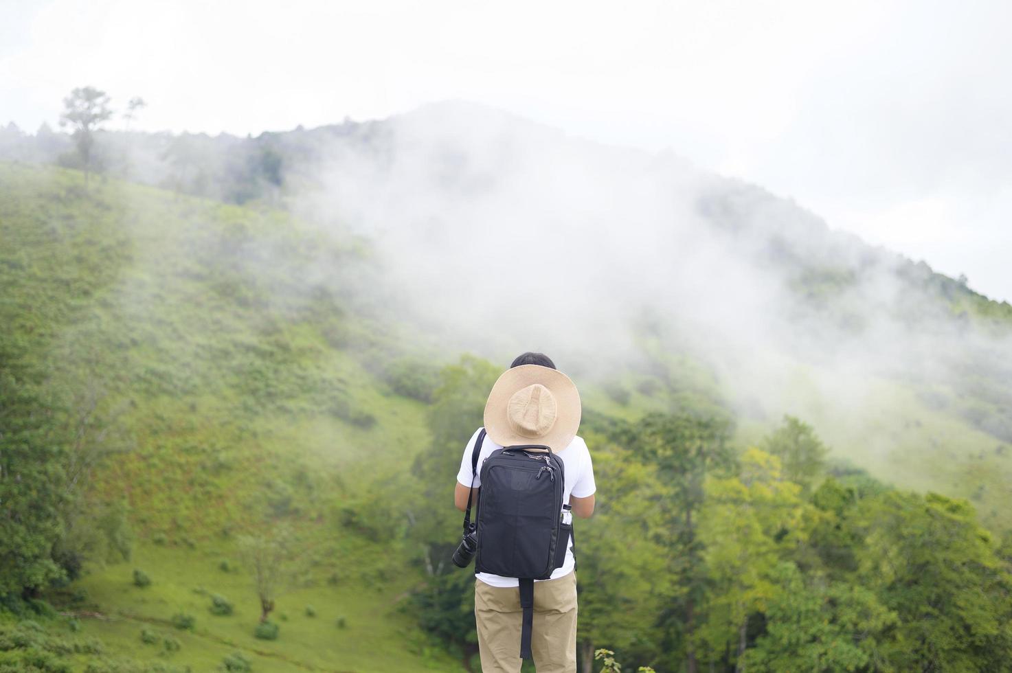 Traveling man enjoying and relaxing over beautiful green mountain view in rain season, Tropical climate. photo