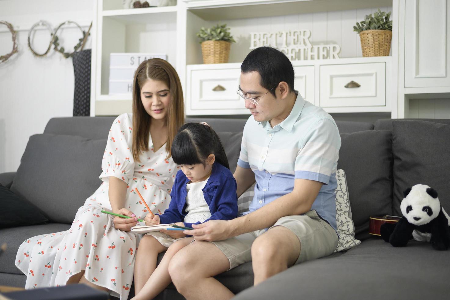 Happy asian parent teaching little cute daughter to do homework and drawing picture together at home. photo