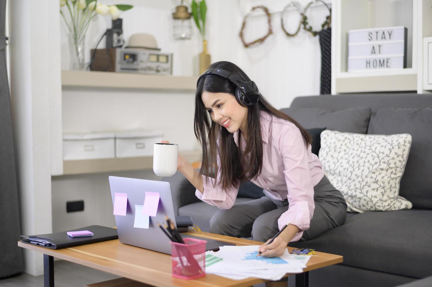 A beautiful young woman wearing headset is making video conference call via computer at home , business technology concept . photo