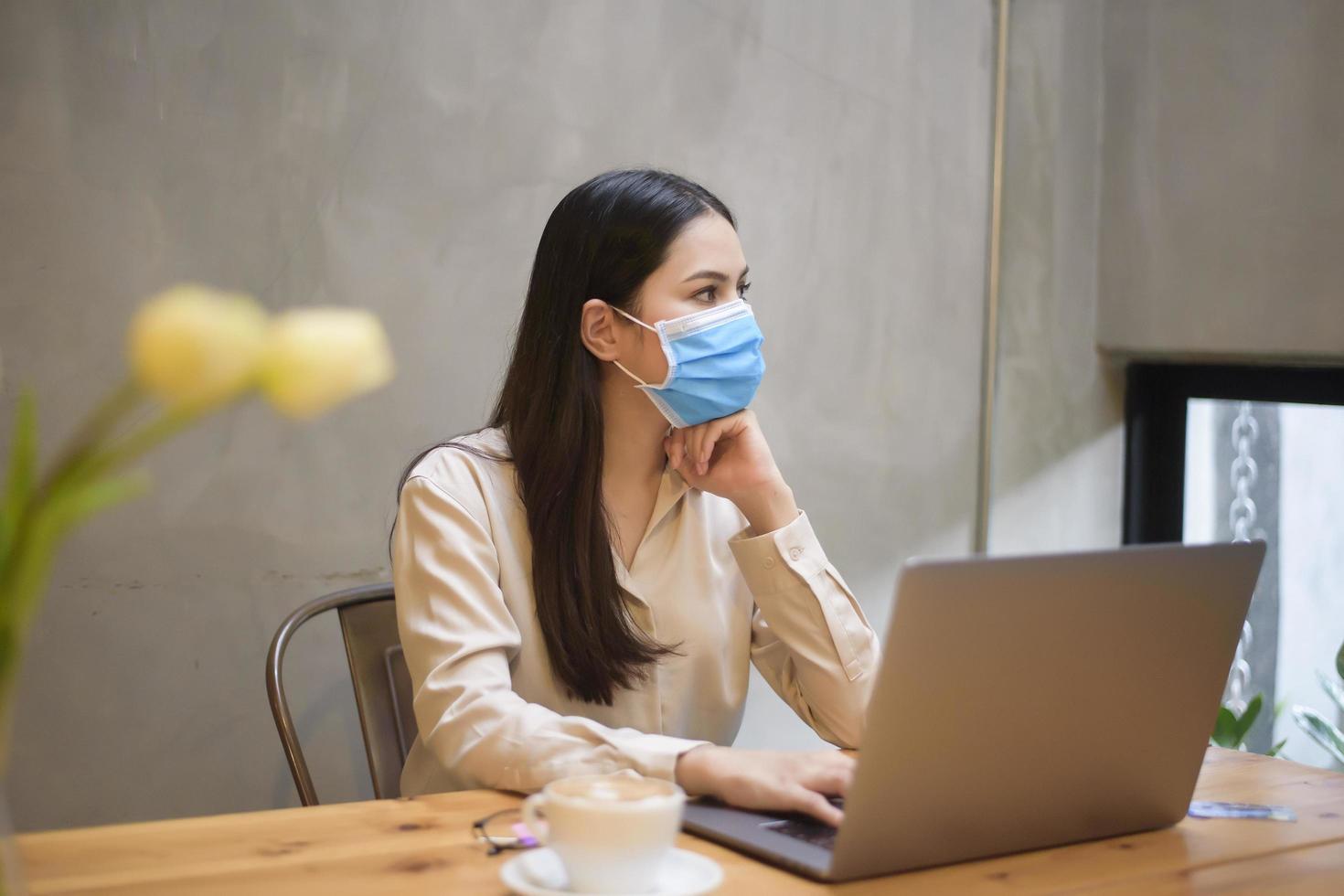 hermosa mujer con máscara está trabajando en una computadora portátil en una cafetería foto