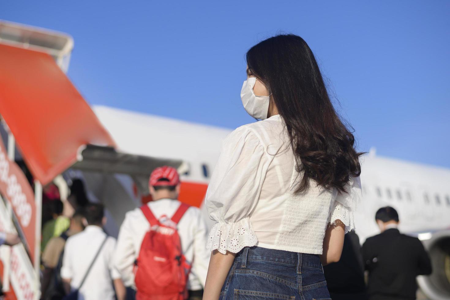 una joven viajera con máscara protectora subiendo al avión y lista para despegar, viajar bajo la pandemia de covid-19, viajes de seguridad, protocolo de distanciamiento social, nuevo concepto de viaje normal foto