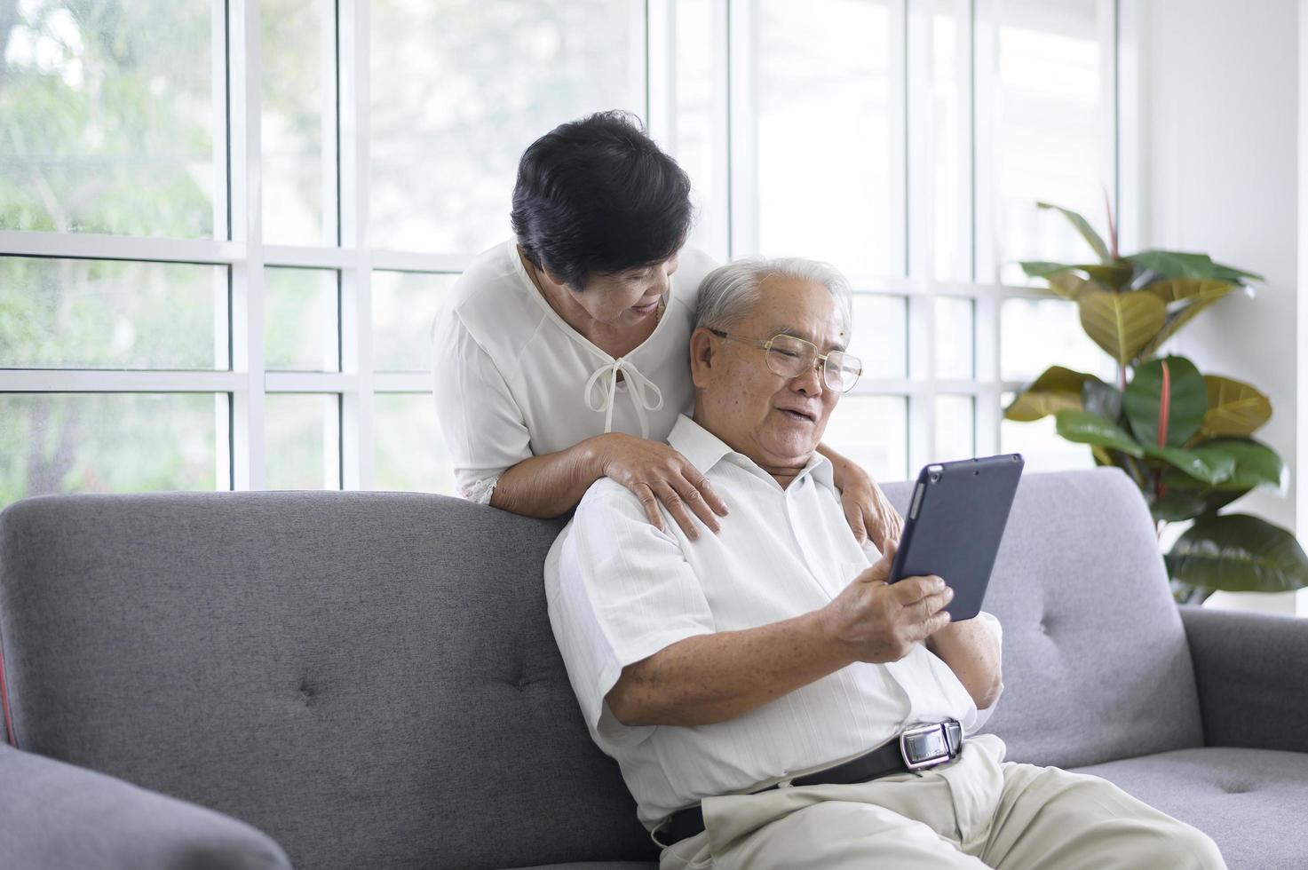 A happy senior Asian couple is using tablet and talking with family on webcam at home, retirement concept. photo