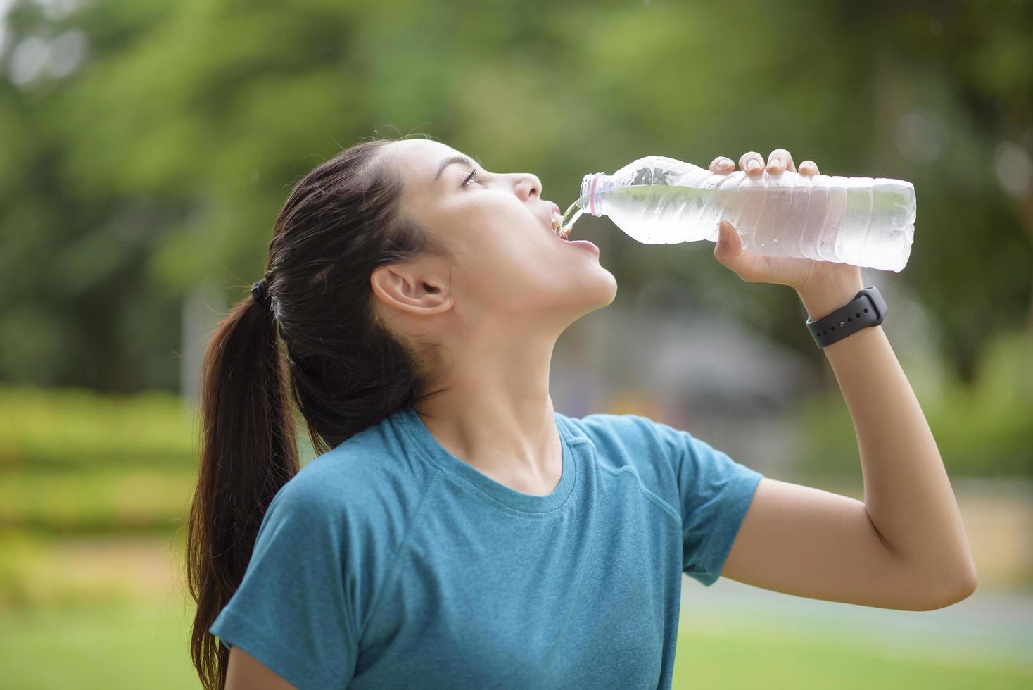 Fitness woman is drinking water after workout in park photo