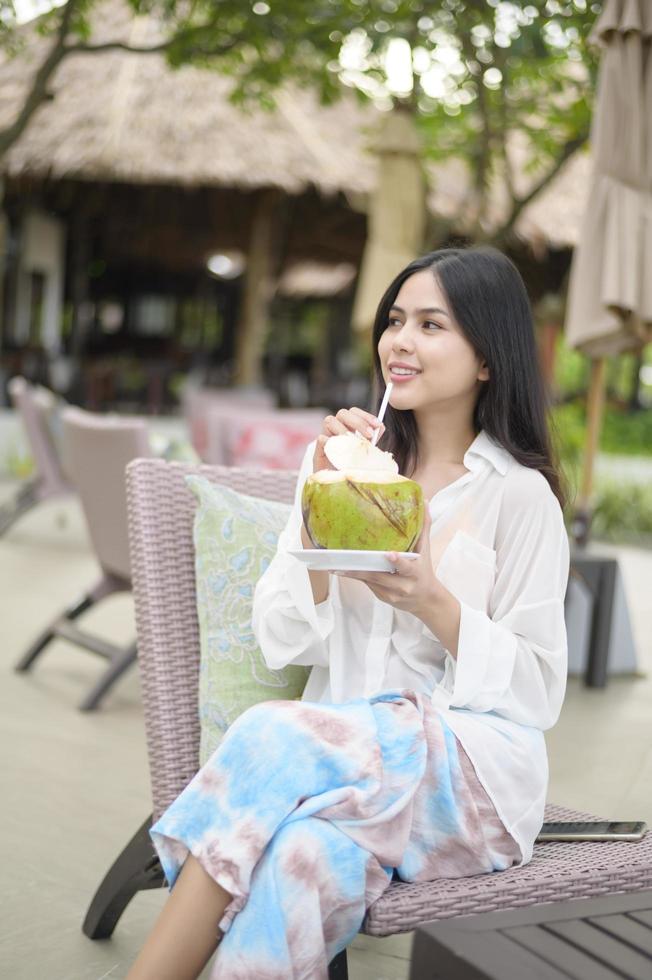 Beautiful woman tourist with white flower on her hair drinking coconut sitting on lounge chair during summer holidays photo