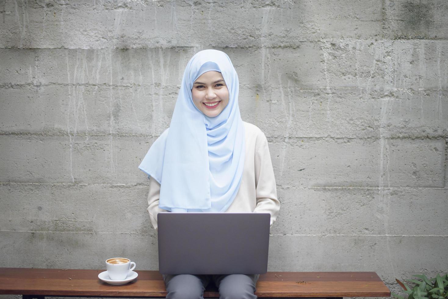 mujer musulmana con hiyab está trabajando con una computadora portátil en una cafetería foto