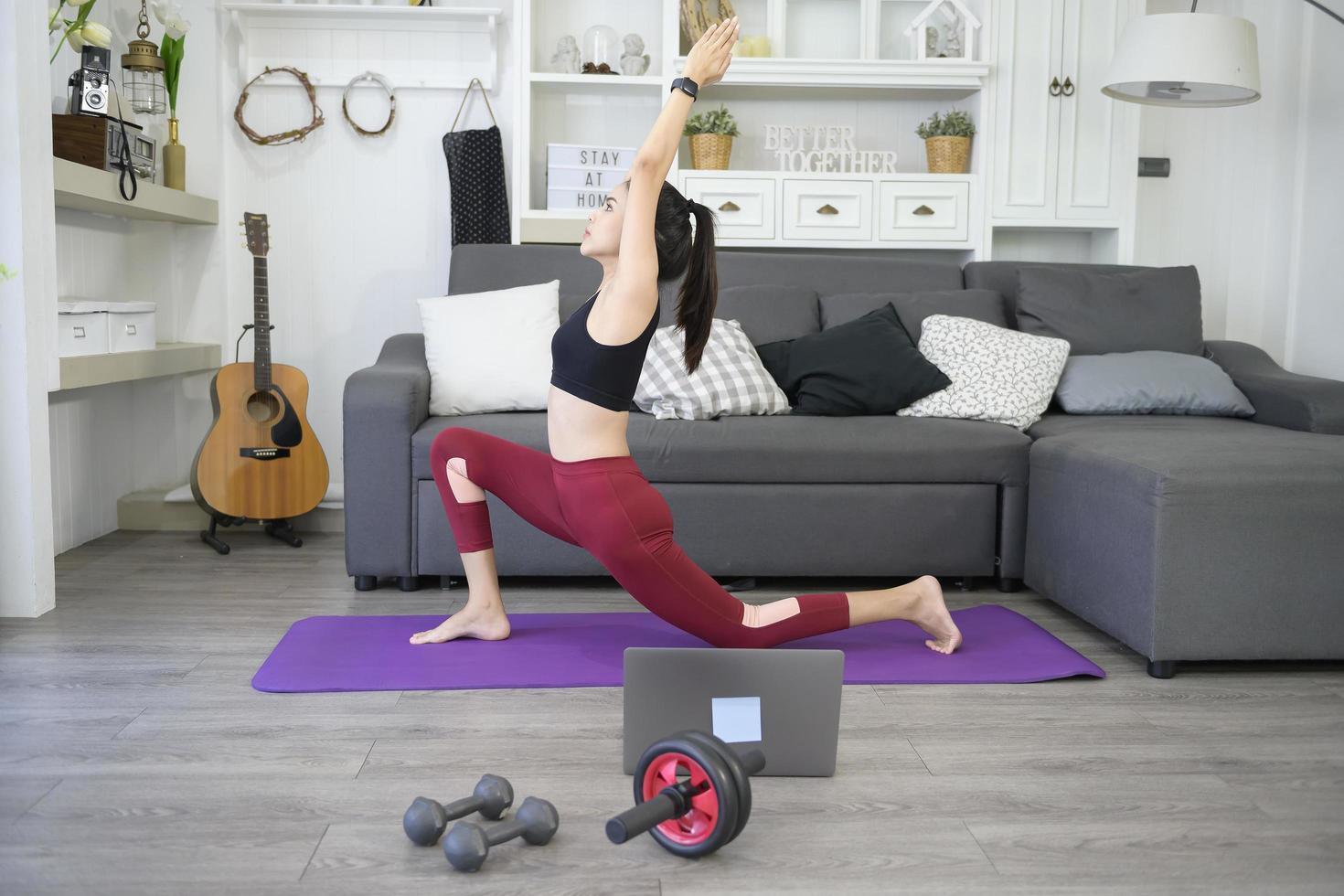 A happy young woman in sportswear is doing stretching and warming up on mat in living room at home photo