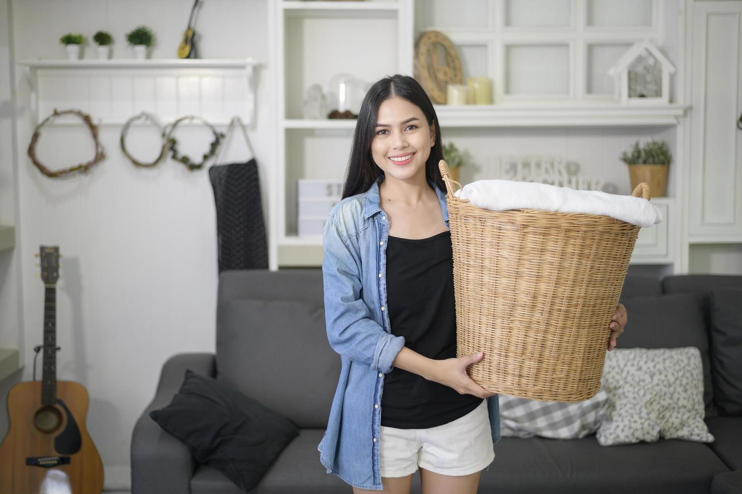 un ama de llaves feliz lleva un cubo de ropa para lavar en la casa. foto