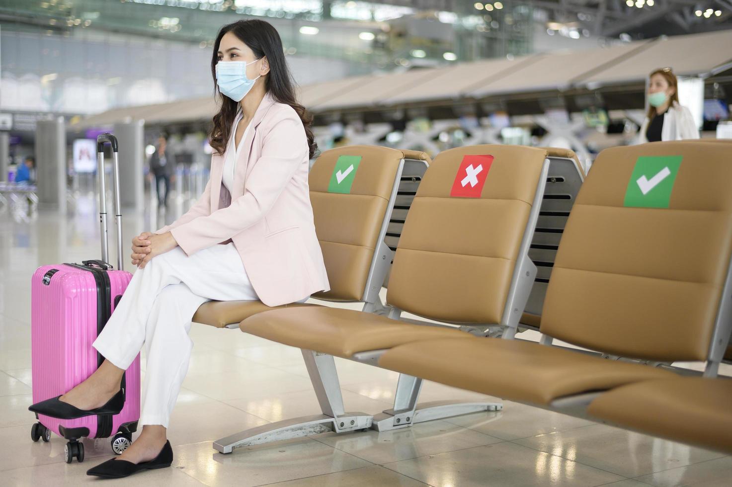 A business woman is wearing protective mask in International airport, travel under Covid-19 pandemic, safety travels, social distancing protocol, New normal travel concept photo