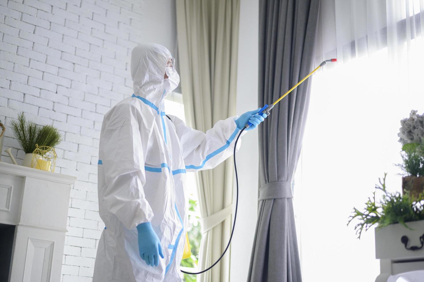 un personal médico con traje de ppe está usando spray desinfectante en la sala de estar, protección covid-19, concepto de desinfección. foto