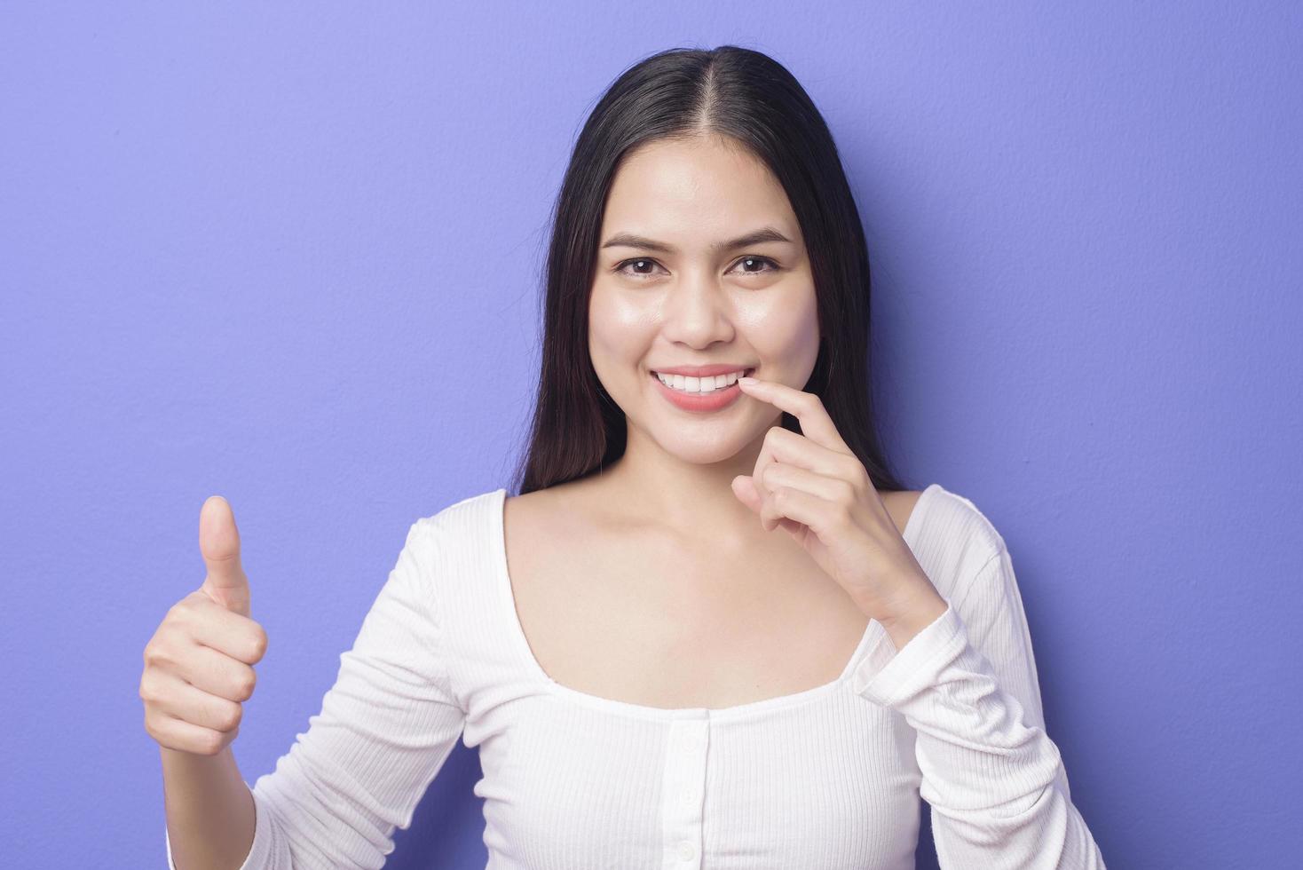 young smiling beautiful woman is showing and pointing her healthy straight white teeth over purple background studio photo