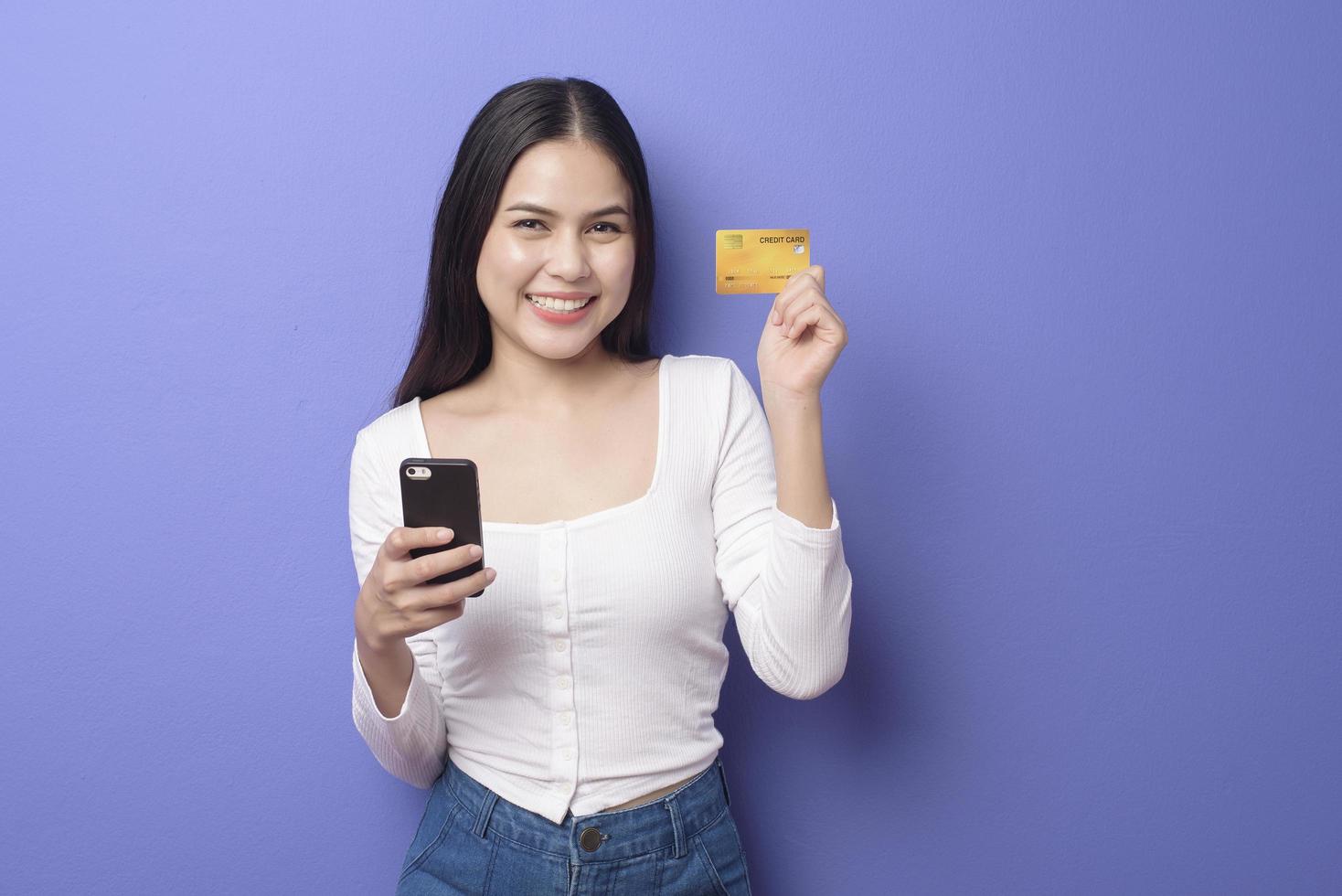 retrato de una joven asiática está usando un teléfono celular con tarjeta de crédito en un fondo morado foto